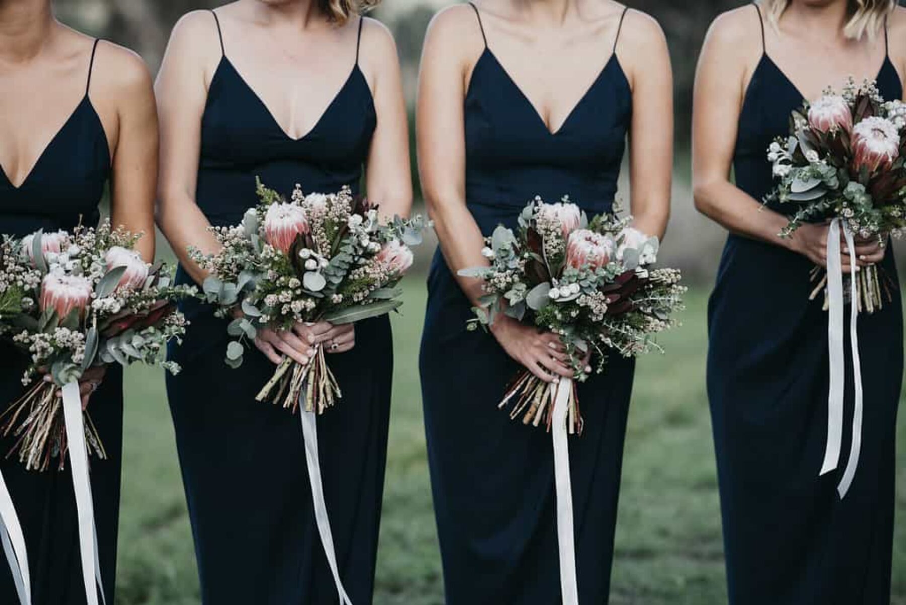 bridesmaids in black dresses with protea bouquets