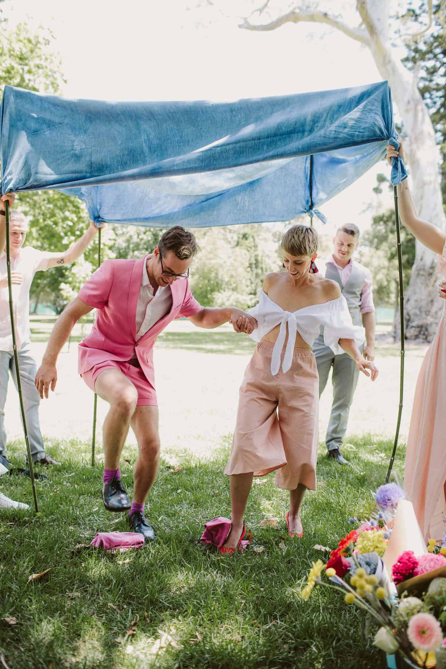 quirky bride and groom in pink, under a blue chuppah