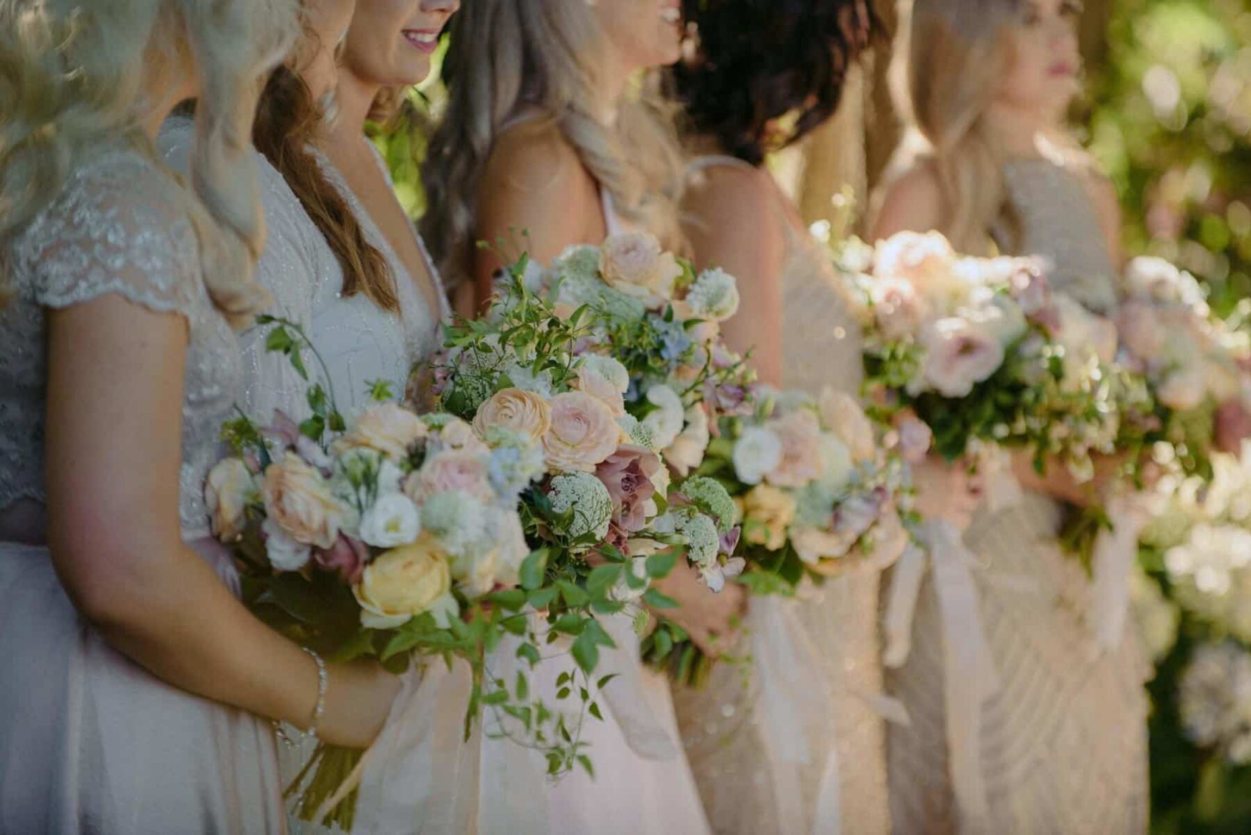 bridesmaids in neutral tones with pastel bouquets