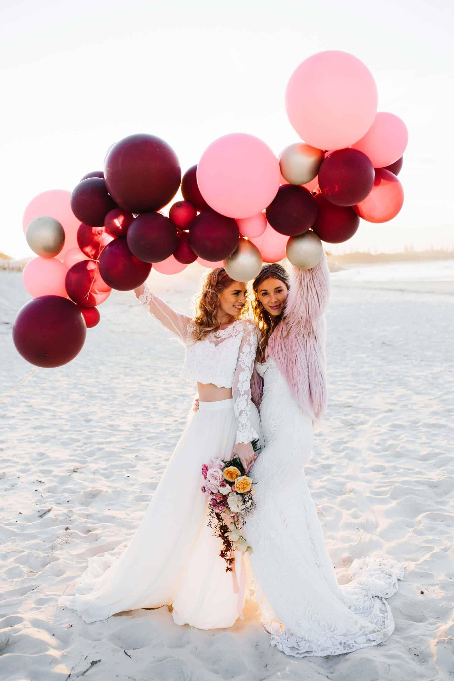brides on the beach with pink balloon garland