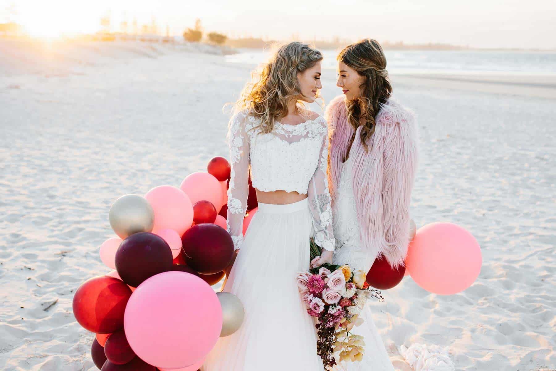 brides on the beach with pink balloon garland