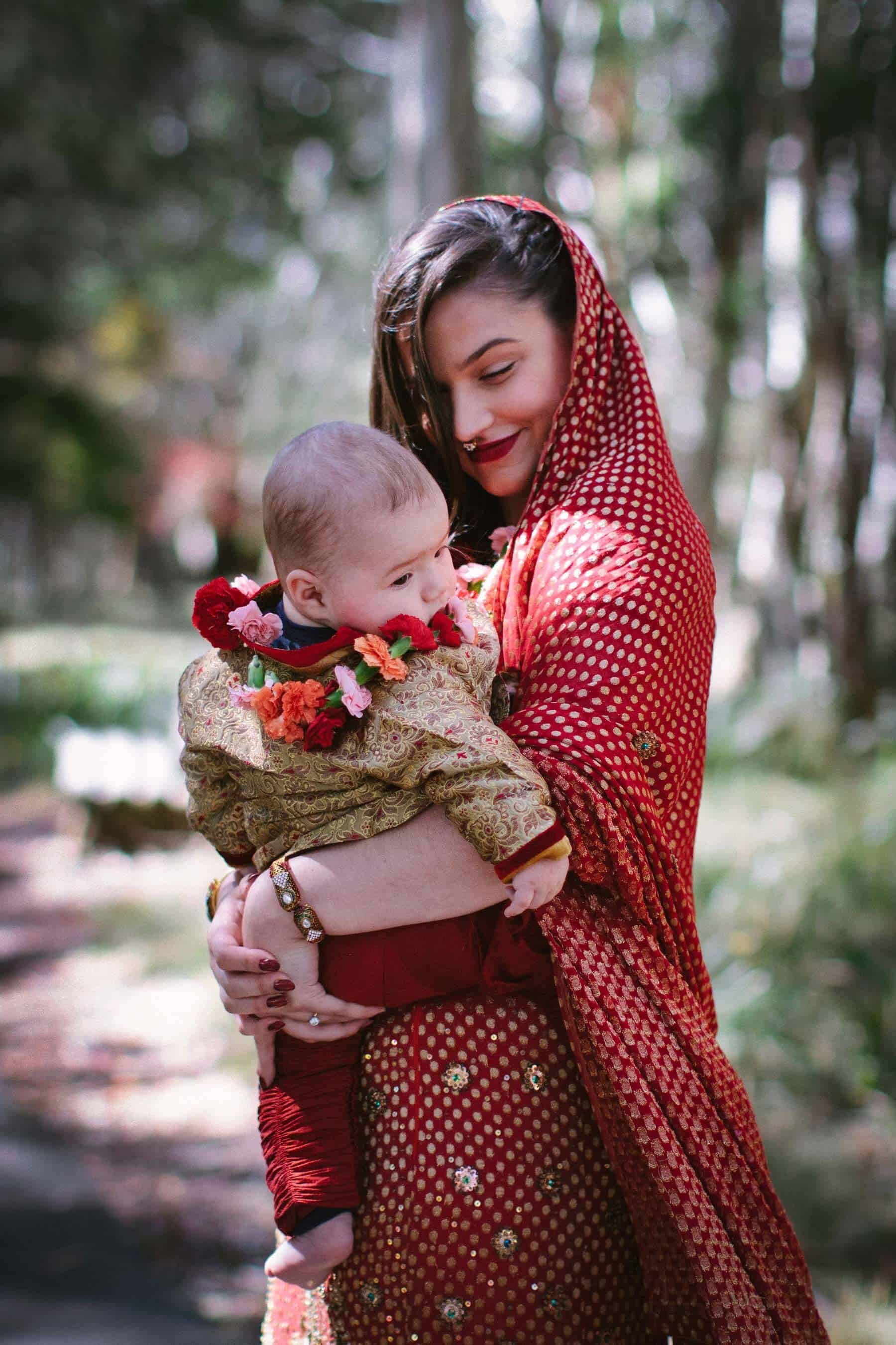bride in a red sari carrying her baby down the aisle