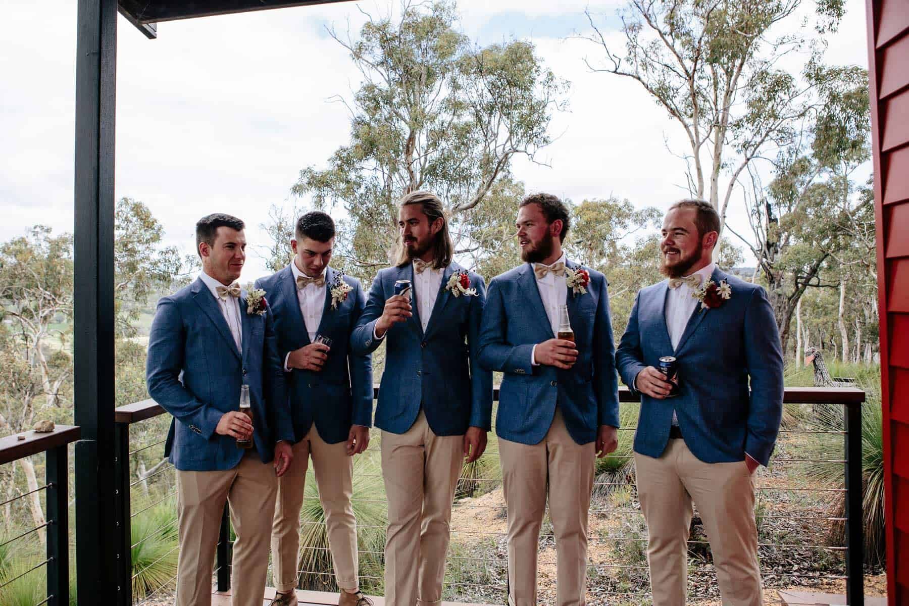 Groomsmen wear navy blazers with red rose Navy blazer with gold bowtie and red rose boutonnière